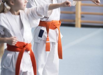 Young girls wearing orange belts, training moves and looking in the direction of their coach during karate classes